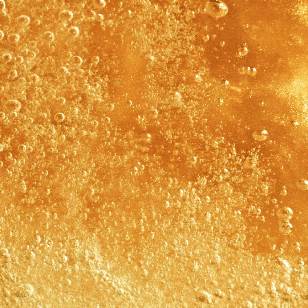 A macro close-up of the bubbly, amber liquid inside a can of Good Shit tropical pre + probiotic soda