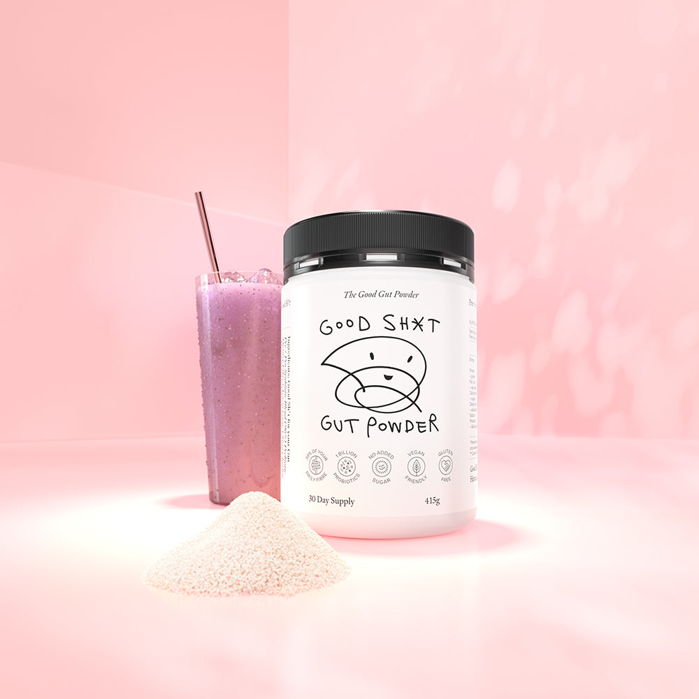 A large tub of Good Shit pre + probiotic Gut Powder, containing enough powder for 30 days, with a frosty glass of berry smoothie with ice behind it. There is a pile of Good Shit pre + probiotic powder in front of the tub.